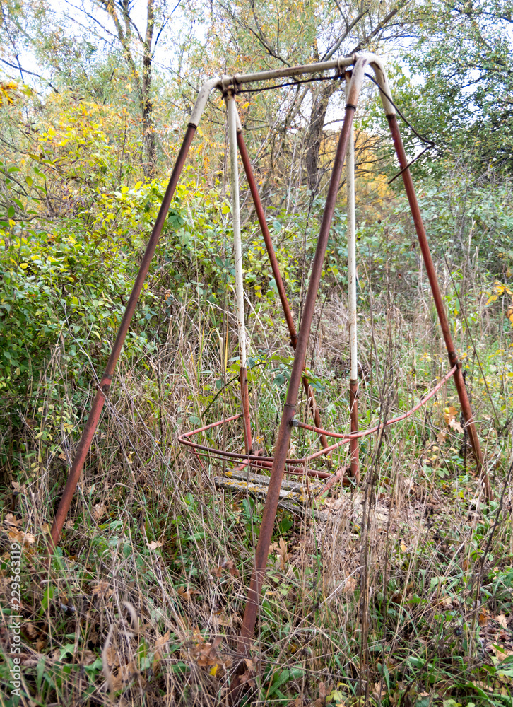 Fototapeta premium Old abandoned rusty swing among grass and trees