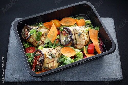 Dieta pudełkowa. Roladki z grillowanego bakłażana z suszonymi pomidorami i serem podane na sałacie i marchewce zapakowane w pojemnik na żywność.