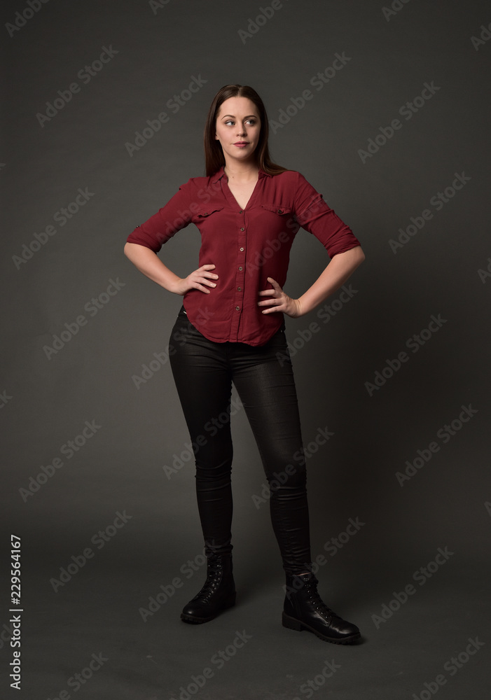 full length portrait of brunette girl wearing red shirt and leather pants. standing pose, on grey studio background. full length portrait of brunette girl wearing red shirt and leather pants. standing pose, on grey studio background.