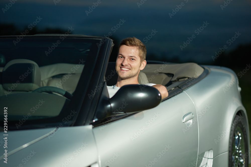 Handsome driver of silver cabriolet looking at camera, smiling. Handsome driver of silver cabriolet looking at camera, smiling.