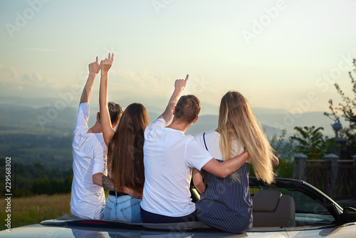 Couples sitting in cabriolet, holding hands up and admiring amazing view.