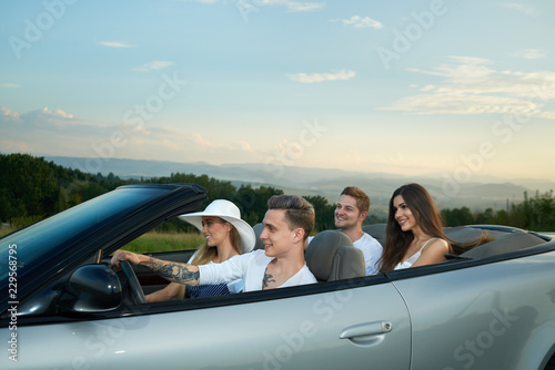 Four friends going for drive, sitting in silver cabriolet.