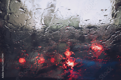 Drops Of Rain Drizzle on the glass windshield in the evening. street in the heavy rain. Bokeh Tail light. soft Focus. Please drive carefully, slippery road. soft focus.