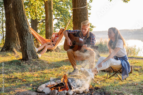 Best friends playing guitar and enjoying at bonfire on picnic on hiking at the lake