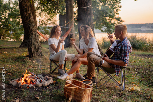 Best friends playing guitar and having fun at bonfire on picnic at the lake