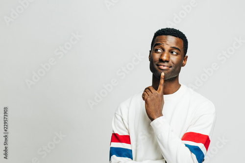 Portrait of a casual young man thinking with his finger on his mouth and looking left, isolated on white studio background