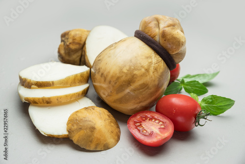 Traditional Italian smoked Scamorza cheese with herbs and tomatoes on gray background.