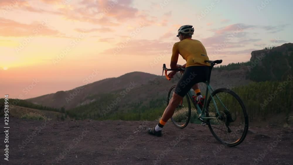 A tourist on a Bicycle admires the sunset from the top of the mountain A tourist on a Bicycle admires the sunset from the top of the mountain