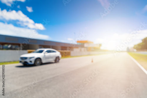 Abstract blur and bokeh. White Luxury car in racetrack and speed racing back ground clear sky. Sunlight and flare concept.