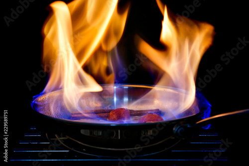 A pan with flames flambeing fruit. Black background.