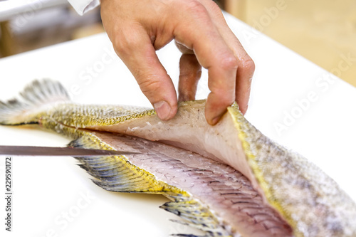 Fotografija A chef filleting a zander with a knife on white chopping board.