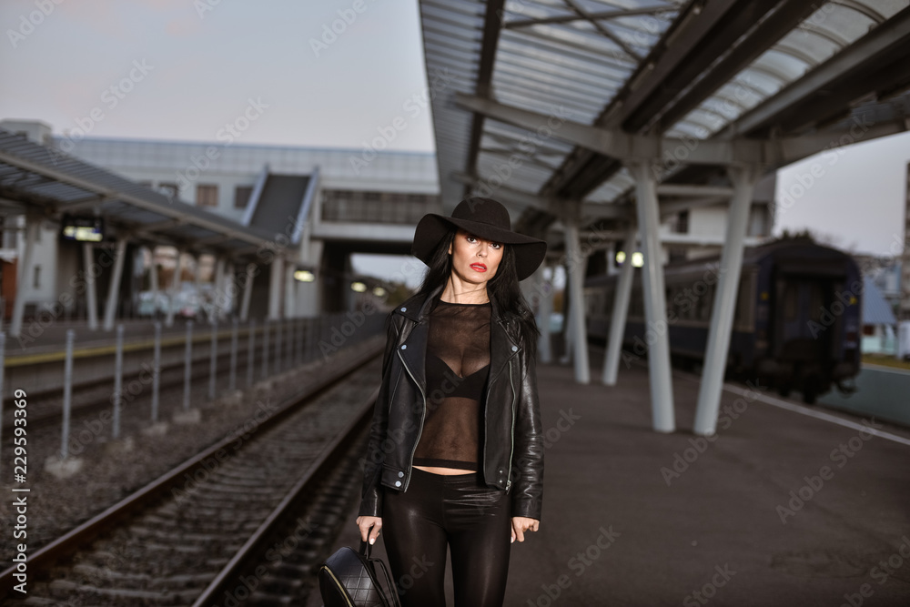 Obraz premium Young sexy woman dressed in black posing on a train station pier.