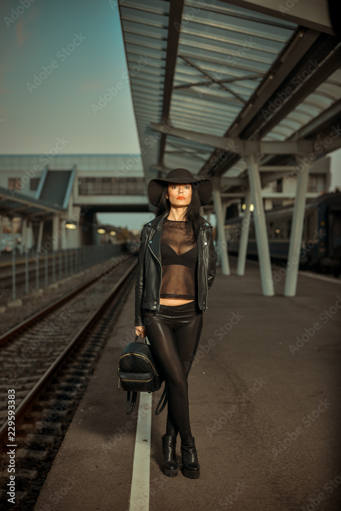 Young sexy woman dressed in black posing on a train station pier.