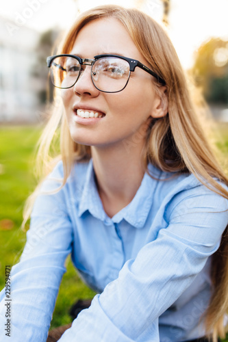Portrait of a cute young girl wearing glasses sitting on the grass in the park