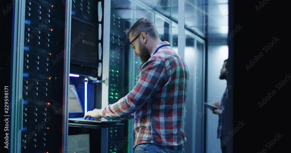 Adult men with laptop and tablet working on diagnostics of servers in contemporary data center