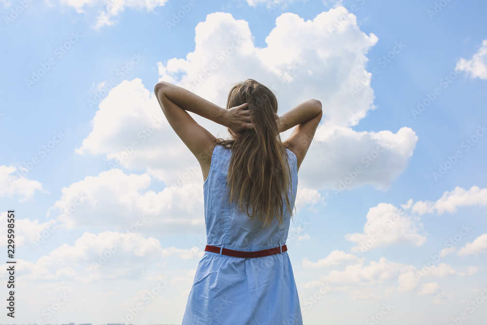 Young hipster girl is travelling in summer holidays. Woman in modern dress is looking at blue sky and white clouds enjoying fresh air and sunbathing. Freedom and lifestyle concept. Beautiful nature. Young hipster girl is travelling in summer holidays. Woman in modern dress is looking at blue sky and white clouds enjoying fresh air and sunbathing. Freedom and lifestyle concept. Beautiful nature.