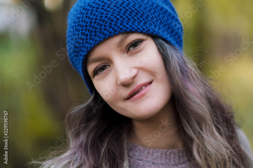 The girl in a coat and blue hat on a background of autumn trees and maple leaves.