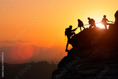 Silhouette of the climbing team helping each other while climbing up in a sunset. The concept of aid. photo