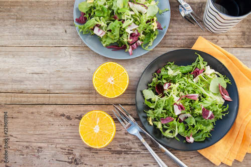 Fresh green salad with spinach, arugula, romaine and lettuce with orange fruit. Rustic wooden table. 