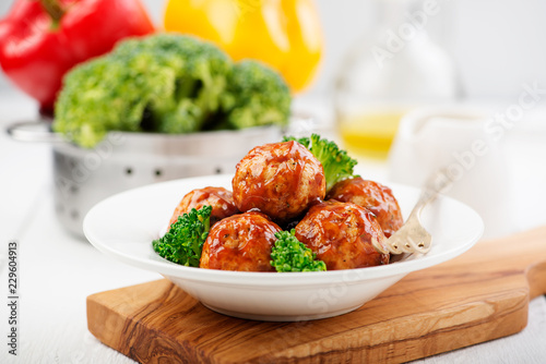 Meatballs with barbeque sauce and broccoli on wooden table.