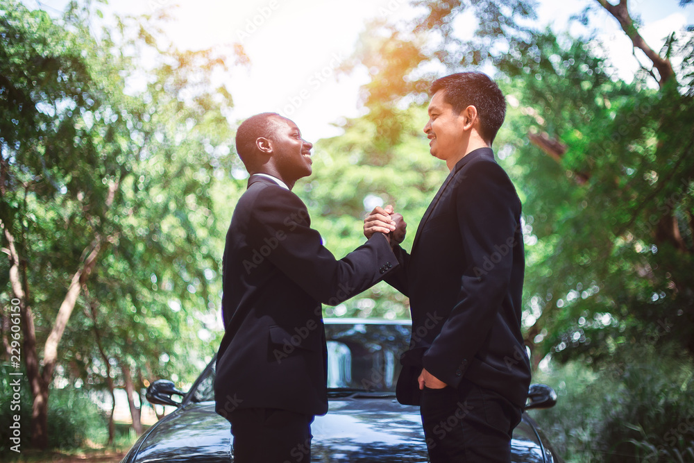 African American businessman and Asian businessman shaking hands after meeting with green natural background. African American businessman and Asian businessman shaking hands after meeting with green natural background.
