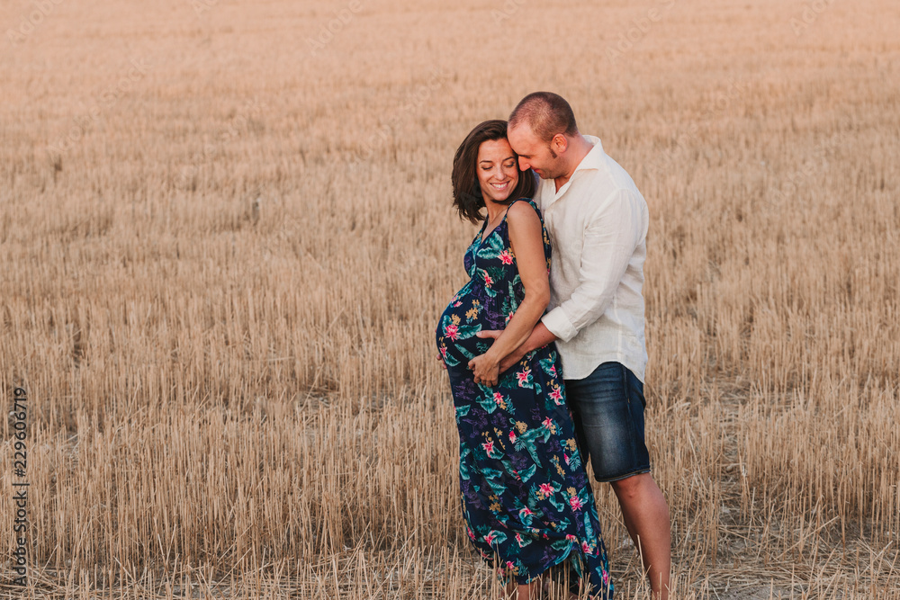 portrait outdoors of a young pregnant couple in a yellow field. Outdoors family lifestyle. portrait outdoors of a young pregnant couple in a yellow field. Outdoors family lifestyle.