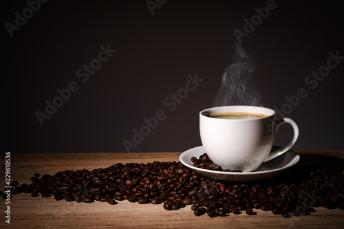 Steaming coffee in cup put on coffee beans on wood background with copy space.