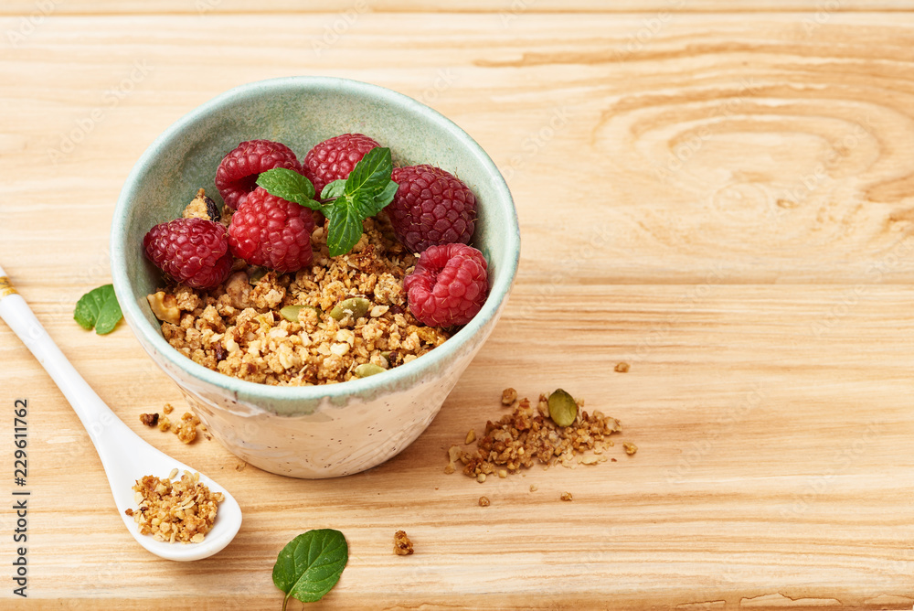 Homemade granola in a bowl with raspberries on a wooden table. Homemade granola in a bowl with raspberries on a wooden table.