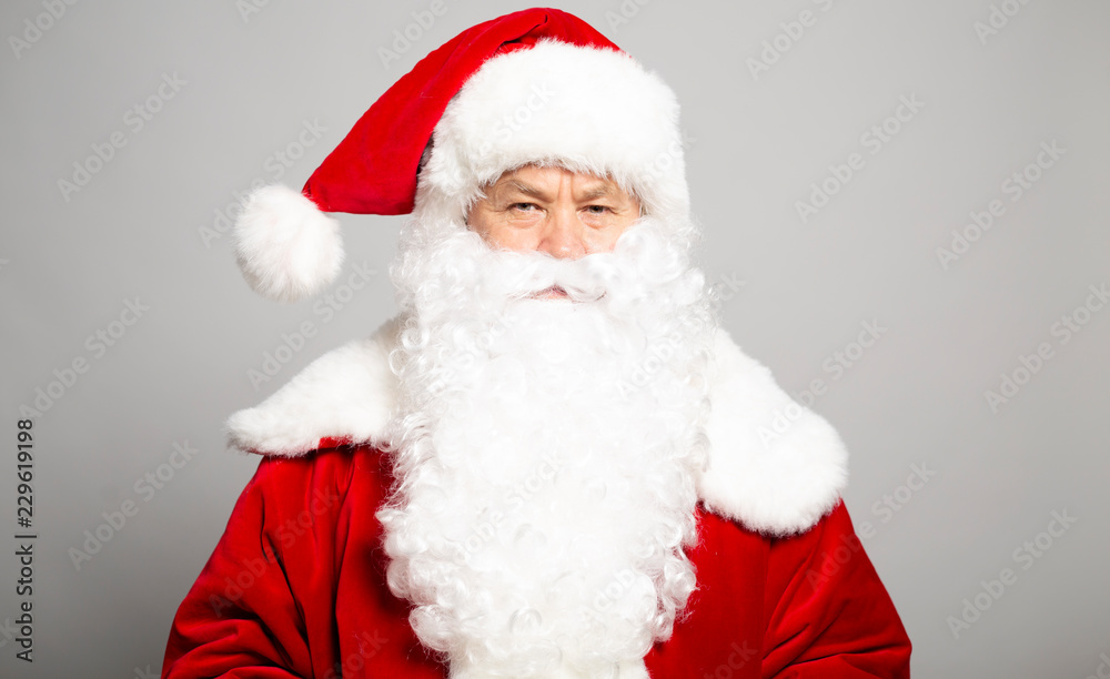 Portrait of serious man in Santa Clause costume looking at camera on grey background, Christmas and New year concept Portrait of serious man in Santa Clause costume looking at camera on grey background, Christmas and New year concept