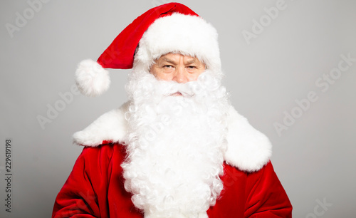 Portrait of serious man in Santa Clause costume looking at camera on grey background, Christmas and New year concept © My Ocean studio