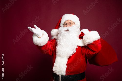 Portrait of grandfather in Santa Clause costume with gift sack on back posing on red background, Christmas and New year concept