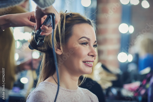 Young beautiful european lady is getting proffessional hair style in a beauty salon. She is smiling.