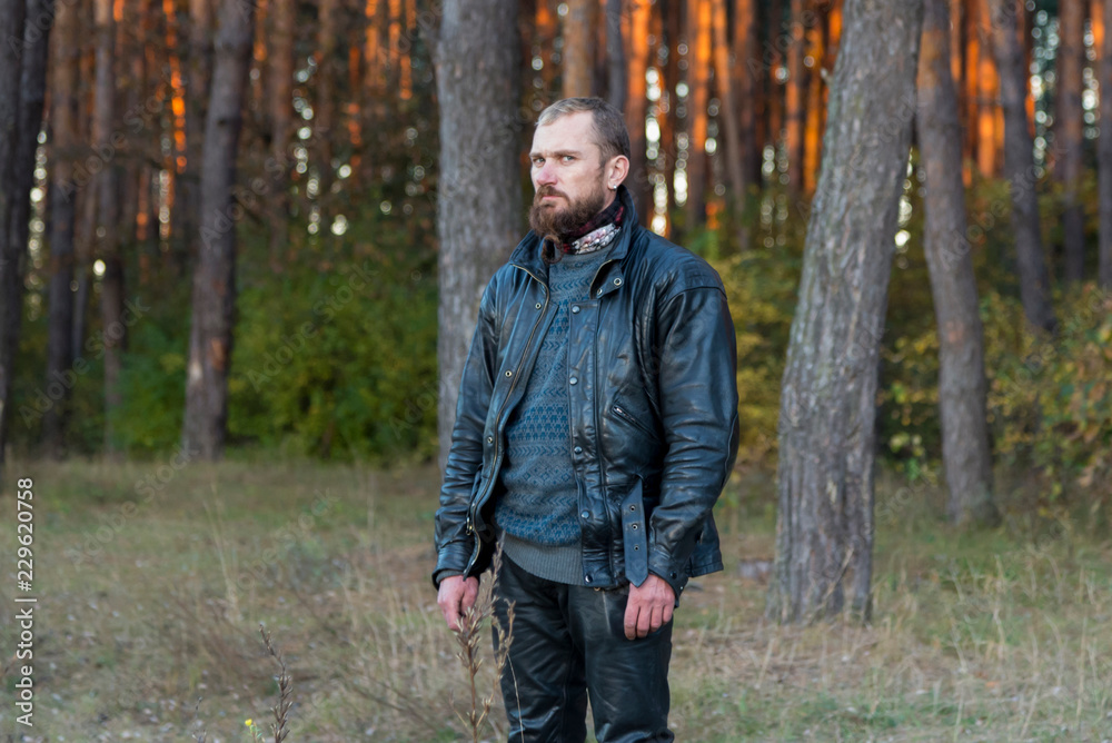 Motorcyclist in a leather jacket and pants standing in a forest