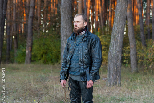 Motorcyclist in a leather jacket and pants standing in a forest
