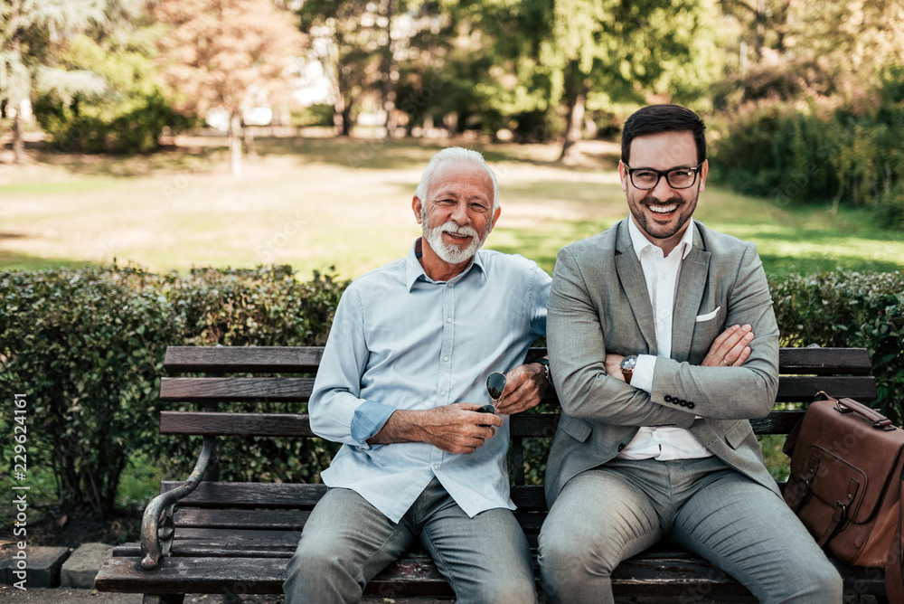 Fototapeta premium Portrait of elegant senior and young man sitting on a bench in the park.