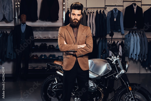 Elegantly dressed man with stylish beard and hair posing near retro sports motorbike at the men's clothing store.