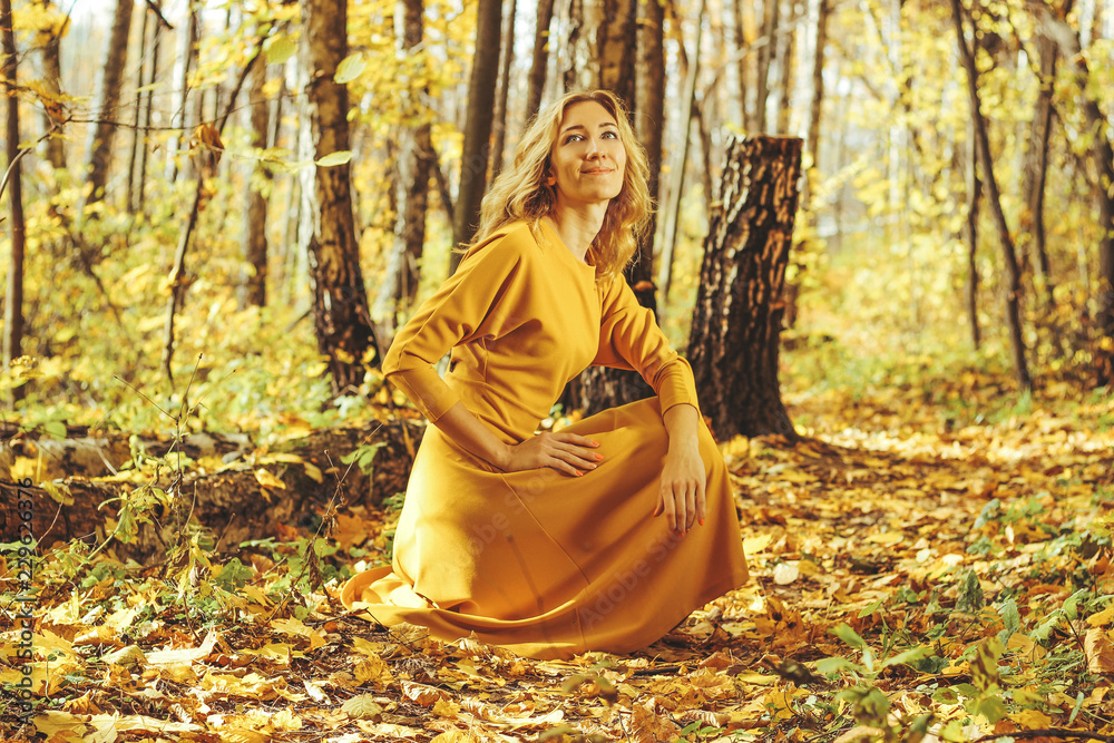 Young beautiful girl in a yellow long dress walks in autumn park with fallen leaves