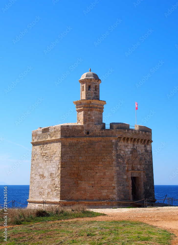 The Sant Nicolau Castle in ciutadella menorca on the cliffs with blue summer sea and blue sky