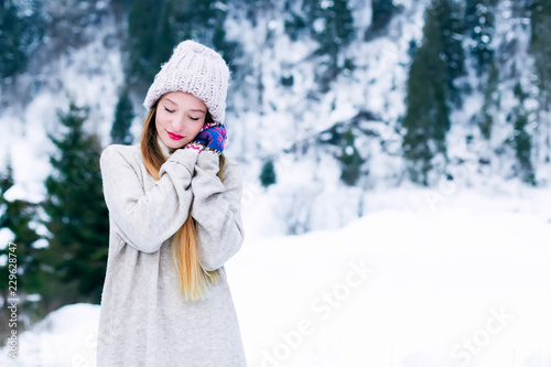 girl in warm clothes closed her eyes and hold her hands around her face against the background of snow-capped mountains