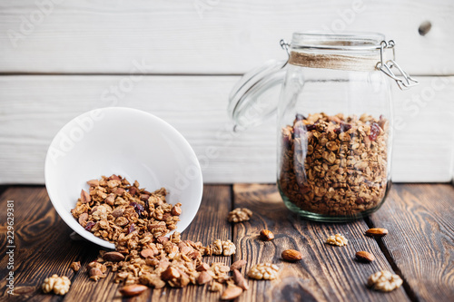 homemade granola in glass jar and scattered on a wooden table.