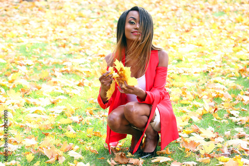 Beautiful young African girl collects autumn leaves in the Park