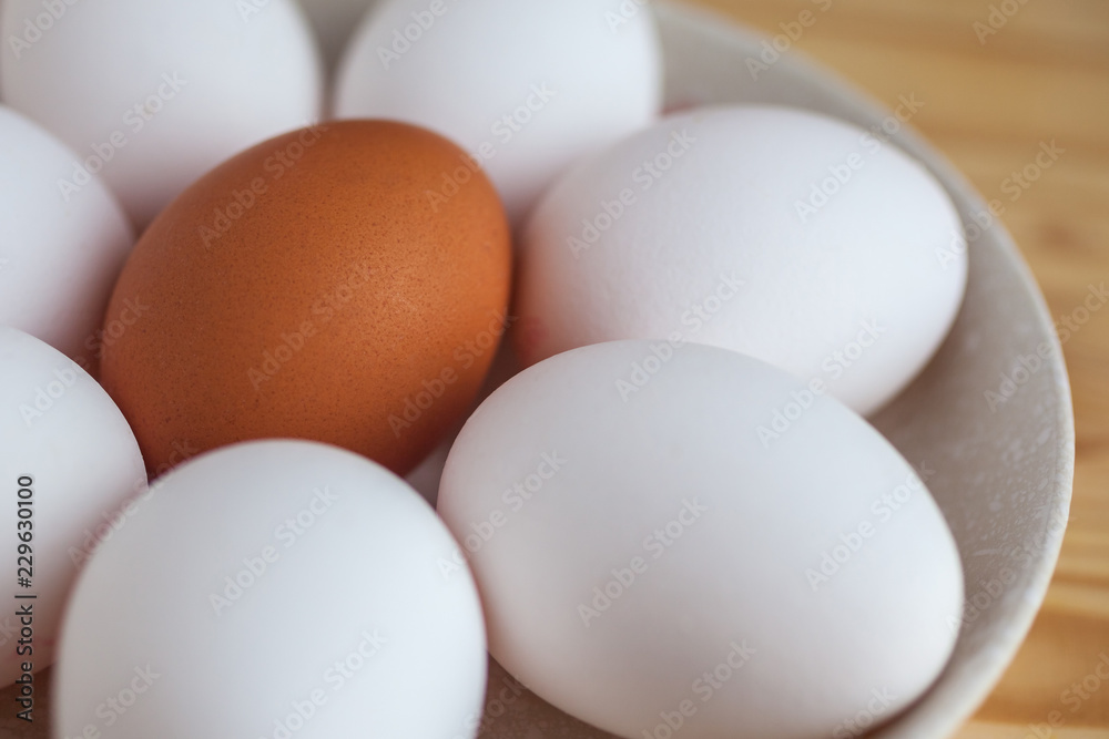 One brown and white eggs in a ceramic dish on a wooden table One brown and white eggs in a ceramic dish on a wooden table