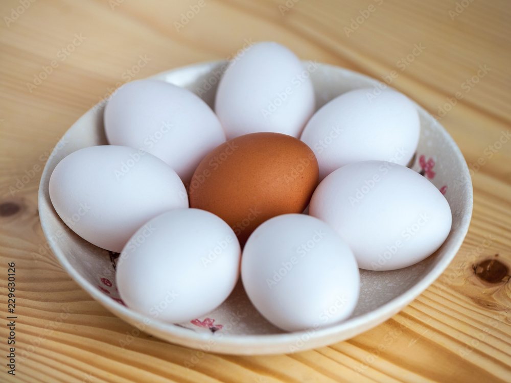 One brown and white eggs in a ceramic dish on a wooden table One brown and white eggs in a ceramic dish on a wooden table