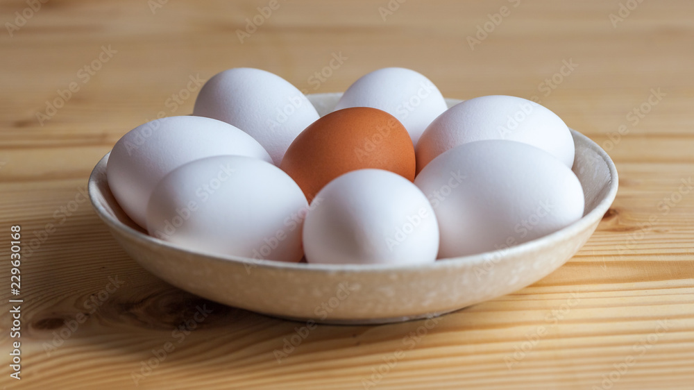 One brown and white eggs in a ceramic dish on a wooden table One brown and white eggs in a ceramic dish on a wooden table