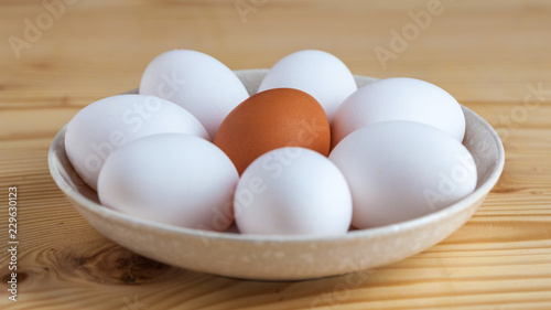 One brown and white eggs in a ceramic dish on a wooden table