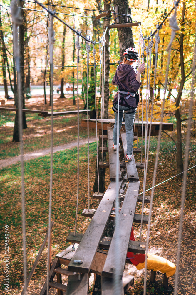 happy girl, women, climbing gear in an adventure park are engaged in rock climbing on the rope road, arboretum, insurance, attraction, amusement park, active recreation, autmn, vertical photo happy girl, women, climbing gear in an adventure park are engaged in rock climbing on the rope road, arboretum, insurance, attraction, amusement park, active recreation, autmn, vertical photo