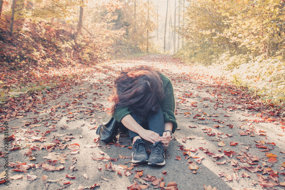 Fototapeta premium Brunette girl sitting on the ground with her head bowed to her knees in the autumn forest, autumn mood concept