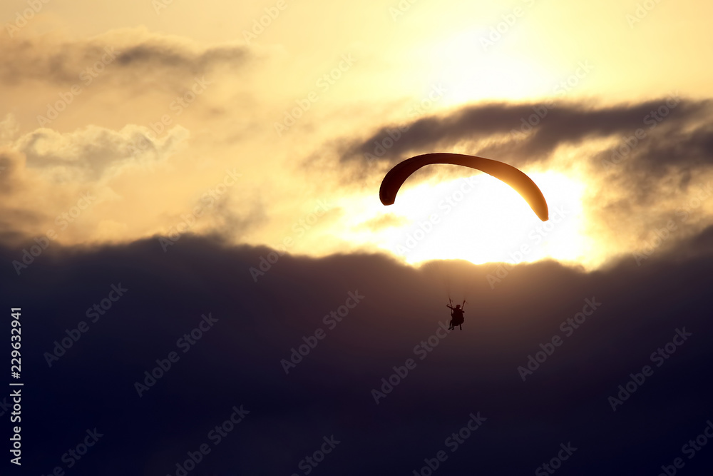 Paraglider flying on a wing in the sky against the setting sun Paraglider flying on a wing in the sky against the setting sun