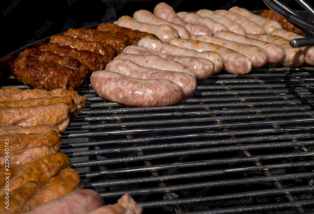 Different meat sausages are fried on a barbecue grid.