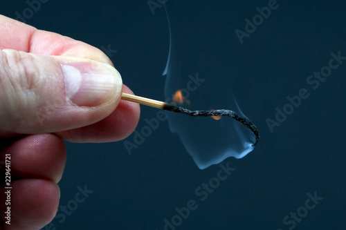 Burning and Smoking wooden match in hand on dark background